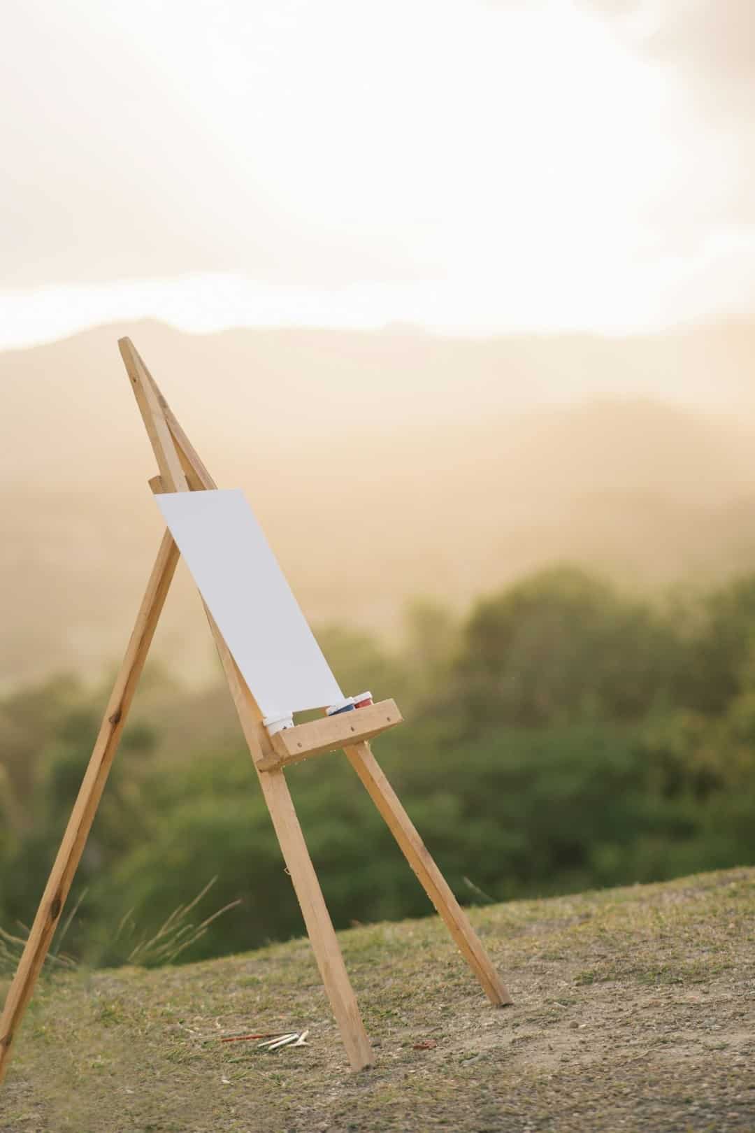 An empty easel and art supplies sit on a grassy hill.